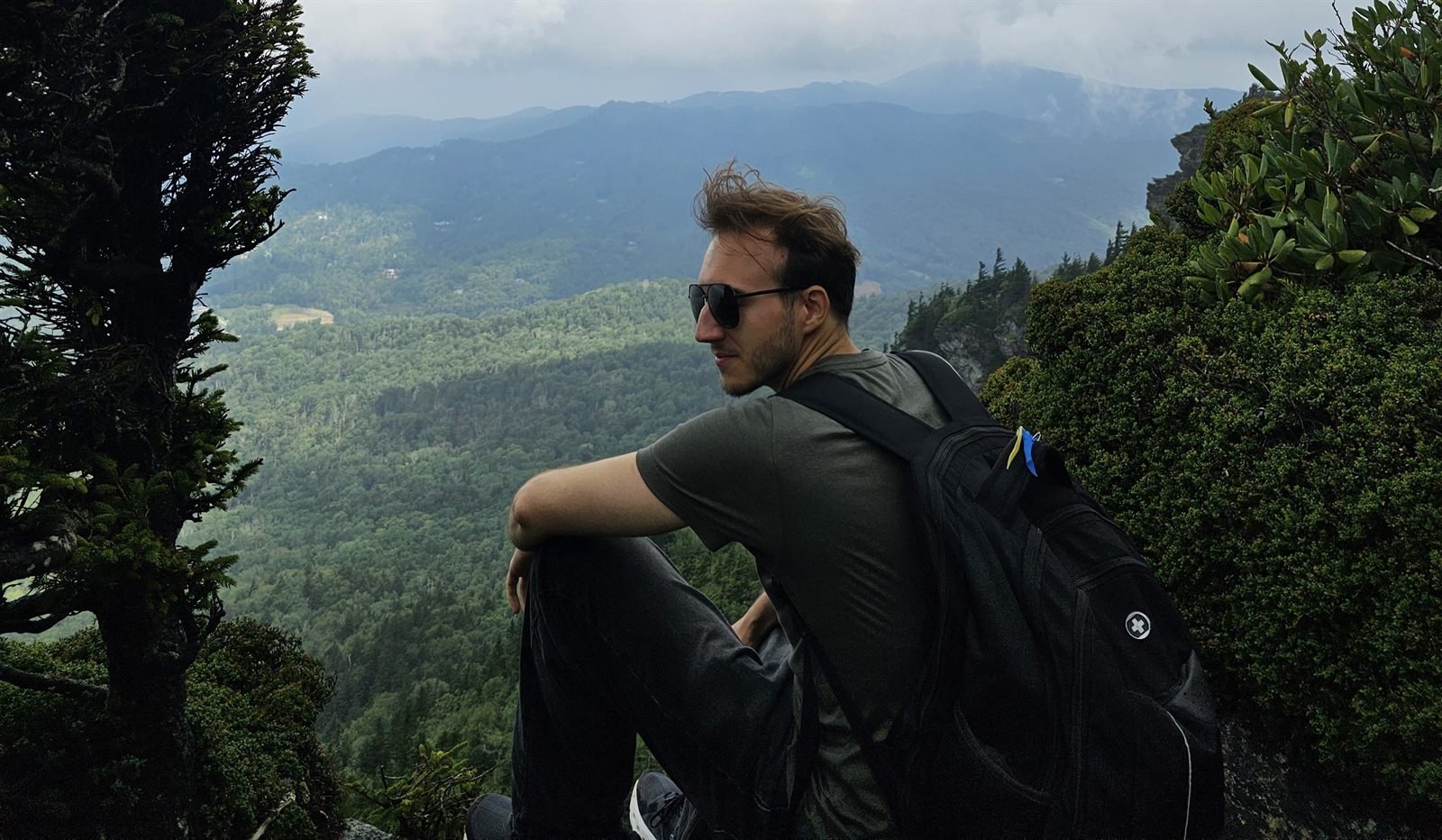 Bogdan Gerasymenko sitting on a rocky ledge above a forested valley